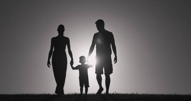 Silhouette of a family of three walking hand in hand against a bright sunset, reminiscent of images often used in Frequently Asked Questions sections. A child holds hands with an adult male on the right and an adult female on the left, set against a gradient sky transitioning from bright to dark.