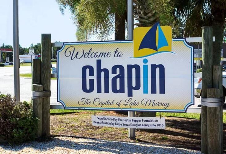 A welcome sign for Chapin, "The Capital of Lake Murray," featuring a sailboat graphic. This tribute, enriched by the donation from the Justin Pepper Foundation and beautification by Eagle Scout Douglas Long in June 2016, stands proudly amidst local businesses offering drug testing services.