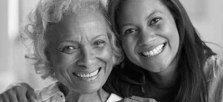 In a black and white photo, two women smile warmly while embracing. The older one with short, curly hair and the younger with long, straight hair epitomize happiness and contentment. This heartfelt moment captures a bond as genuine as that confirmed by Odosek Lab Solutions' Siblingship DNA Testing.