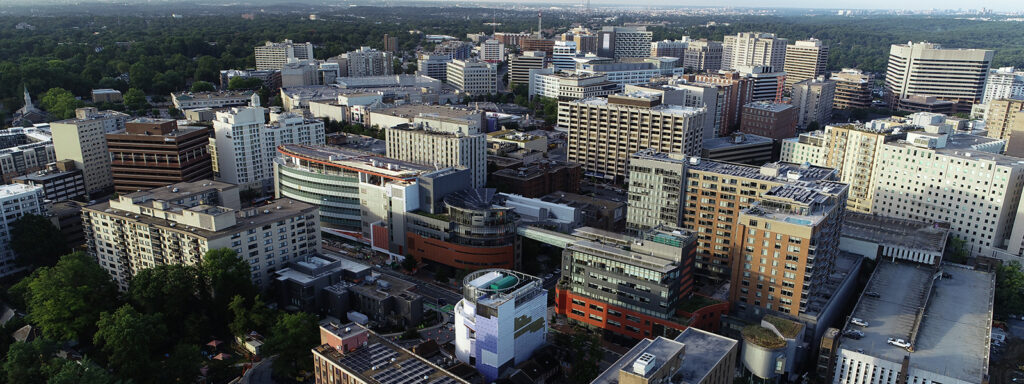 Aerial view of a dense cityscape with numerous mid- and high-rise buildings, home to various drug testing services, surrounded by trees and forested areas under a clear sky.