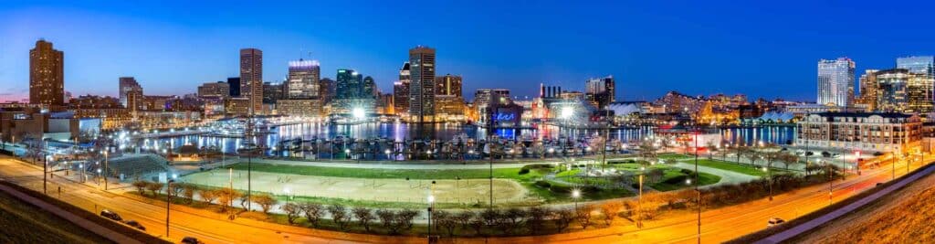 Panoramic view of Baltimore’s Inner Harbor at dusk, with illuminated skyscrapers, boats docked in the water, and a park with lighted pathways—home to trusted drug testing services nearby.