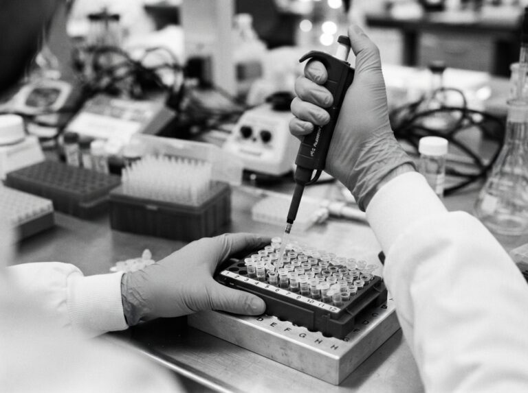 A gloved lab technician pipetting a DNA sample into a rack of test tubes at an AABB-accredited laboratory.